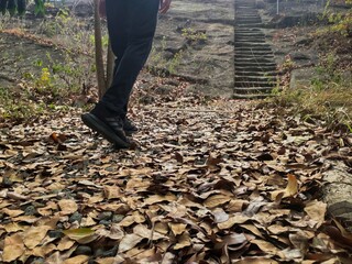 A young man walks along a rocky path covered with dry leaves in the hills.
