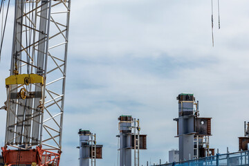 Modern construction site showcasing steel beams forming base structural framework for high-rise building and partial view of heavy duty arm of tall crane with crane hook wires dangling over worksite.