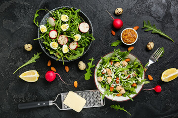 Bowls with tasty arugula salad and ingredients on black grunge background