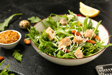 Bowl with tasty arugula salad on black grunge background, closeup