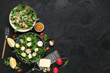 Bowls with tasty arugula salad and ingredients on black grunge background