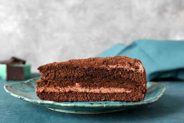 Plate with piece of tasty chocolate cake on blue table in kitchen, closeup