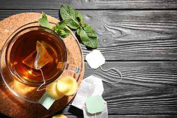 Cup of tasty black tea with ginger and mint leaves on black wooden background, closeup
