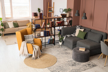 Comfortable armchair, sofa and book shelf in interior of living room, closeup