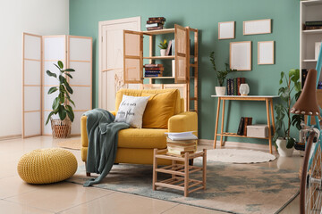 Comfortable armchair, book shelf and table in interior of living room, closeup
