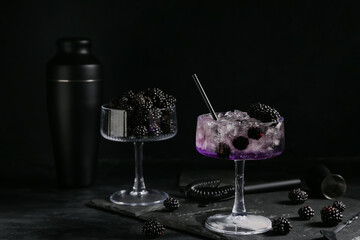 Tray, shaker, glasses with tasty cool blackberry lemonade and ingredient on black background, closeup