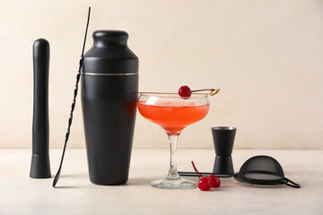 Different bartender utensils and glass with cherry cocktail on beige grunge background