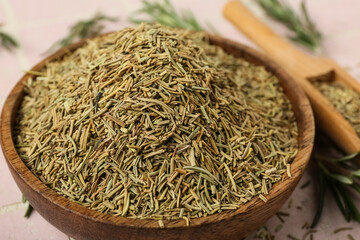 Wooden bowl with dried rosemary on pink tile background, closeup