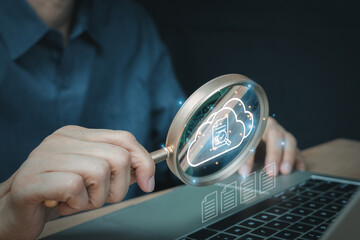 Businessman's hand holding a magnifying glass to audit and verify online documents in a cloud computing system. Concept of data management, information security, and quality assurance technology. © Ben_24