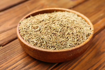Bowl with dried rosemary on wooden background, closeup