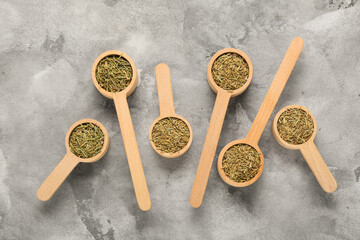 Wooden scoops with dried rosemary on grey grunge background, closeup