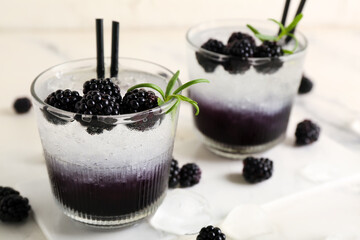 Glasses with tasty cool blackberry lemonade on marble background, closeup