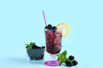 Glass with tasty cool blackberry lemonade and ingredients on blue background