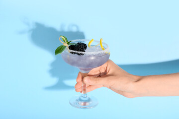 Female hand holding glass with tasty cool blackberry lemonade on blue background, closeup © Pixel-Shot