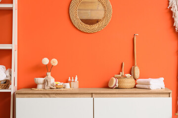 Wicker box, massage body brushes and bottles of cosmetic products on chest of drawers in room,...