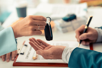 A male car dealer is handing over keys to a customer who has bought or leased a car. and give...