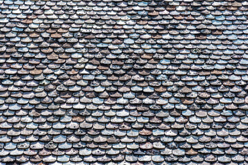 Naklejka premium Close-up shot of an old roof covered in weathered, textured tiles. The aged tiles display varying shades of brown, gray, and blue