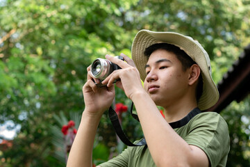 A young man in a boonie hat is taking a photo with his camera, looking focused and passionate about...