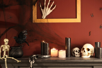 Skulls with burning candles on fireplace in dark room decorated for Halloween