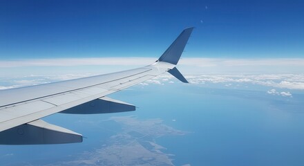 Obraz premium High-altitude view of an airplane wing and tail extending across the vast expanse of a partly cloudy sky, overlooking a body of water.