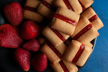 Cookie bars with strawberry jam with fresh strawberries  pn a black plate and over a blue table