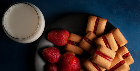 Cookie bars with strawberry jam on a black plate over a blue table with a glass with cold milk on the side panoramic flat lay or top view