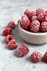 Frozen Raspberries in a Bowl and Scattered on a Textured Gray Surface. Healthy Eating Concept.