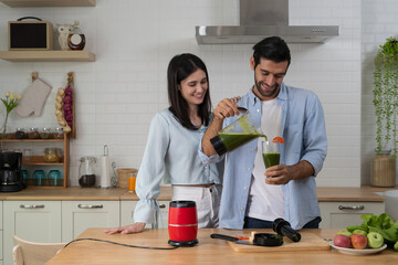 Couple blending fresh green smoothie with vegetables in red blender together in kitchen for healthy living