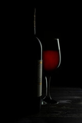 Baroque Renaissance still life with chiaroscuro, a bottle of red wine with a glass on one side and a very dark background, on a rustic wooden table.