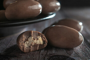 Walnut covered in milk chocolate on a dark plate and a rustic wooden table. Macro photography. Foods high in sugar and carbohydrates with many calories. side view close up
