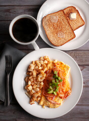 Breakfast with egg, French fries, ham, and tomato sauce on a rustic wooden table, with a fork on a napkin and a cup of black coffee on the side top view  flat lay