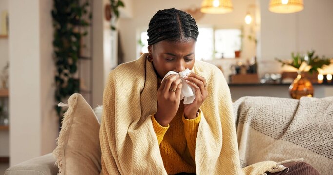 Sick, black woman and blowing nose with tissue on sofa for influenza, allergy or sinus in home. Female person, flu or cold with toilet paper for viral infection, mucus or hayfever on couch in house