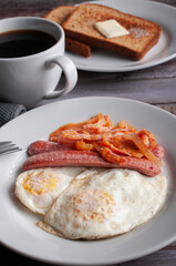  fried overeasy or over medium eggs with sausage, onion, and natural tomato sauce on a white plate, with a fork on the side, well done with toast with butter on a white plate black coffee angle view