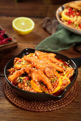 Spicy Asian chicken feet with lemon and peppers in black serving bowl on rustic wooden table