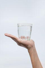 A hand holding a clear glass filled with water against a white background.