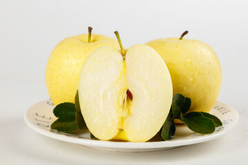 Fresh Yellow Aomori Apples Cut in Half on White Plate with Green Leaves