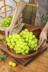 Fresh Green Seedless Grapes in Wicker Basket on Wooden Table with Woman's Hands