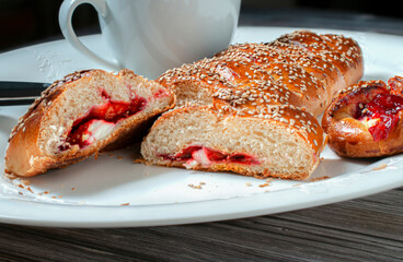 Mexican sweet bread called PAN DE BODA from OAXACA. with sesame seeds on top and filled with cream cheese and strawberry jam with a white cup on a Christmas plate