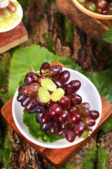 Fresh Red Grapes from Yunnan Vineyard in White Bowl on Rustic Wood Background with Green Leaves