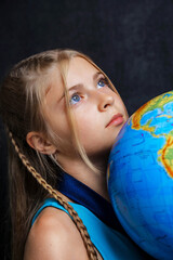 Portrait of a girl with blue eyes, thoughtfully looking upward and holding a globe. A symbol of childhood, dreams of the future, and the desire to explore the world.