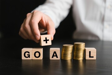 A close-up of a person's hand placing a block labeled '+' next to the word 'GOAL'.