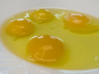 Four raw eggs with yolks and whites in a white bowl, close-up view of fresh ingredients for cooking or baking.