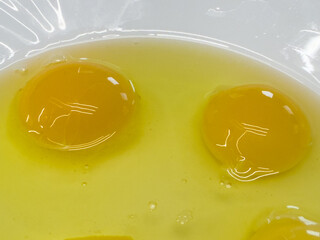 Two raw eggs with yolks and whites in a white bowl on wooden table, close-up ingredient for cooking or baking.