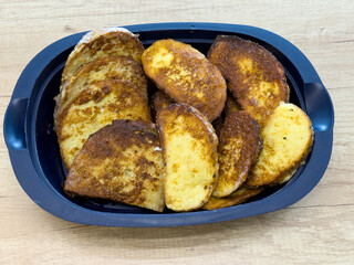 Fried bread slices with golden brown surface served in a black tray on wooden table, homemade meal.