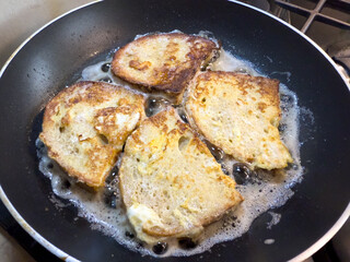 Slices of bread frying in hot oil in a pan, close-up view of golden brown toast preparation.
