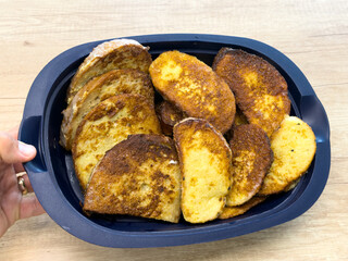 Fried bread slices with golden surface in black tray on wooden table, homemade meal close-up.