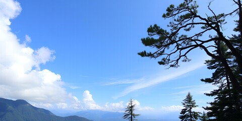 Majestic mountain range under a vast clear blue sky with scattered white clouds and silhouetted pine trees