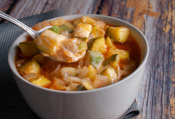 Zucchini soup with melted cheese, tomatoes, and onions seasoned with ingredients and chili, in a white bowl on a rustic wooden table. Spicy Mexican food. angle view