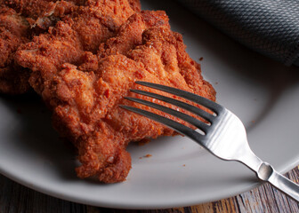 Breaded chicken on a white plate with a fork, high calorie foods macro photography side view