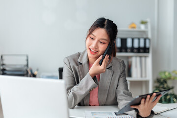 Smiling businesswoman talking on phone and holding tablet while working with documents and laptop in office